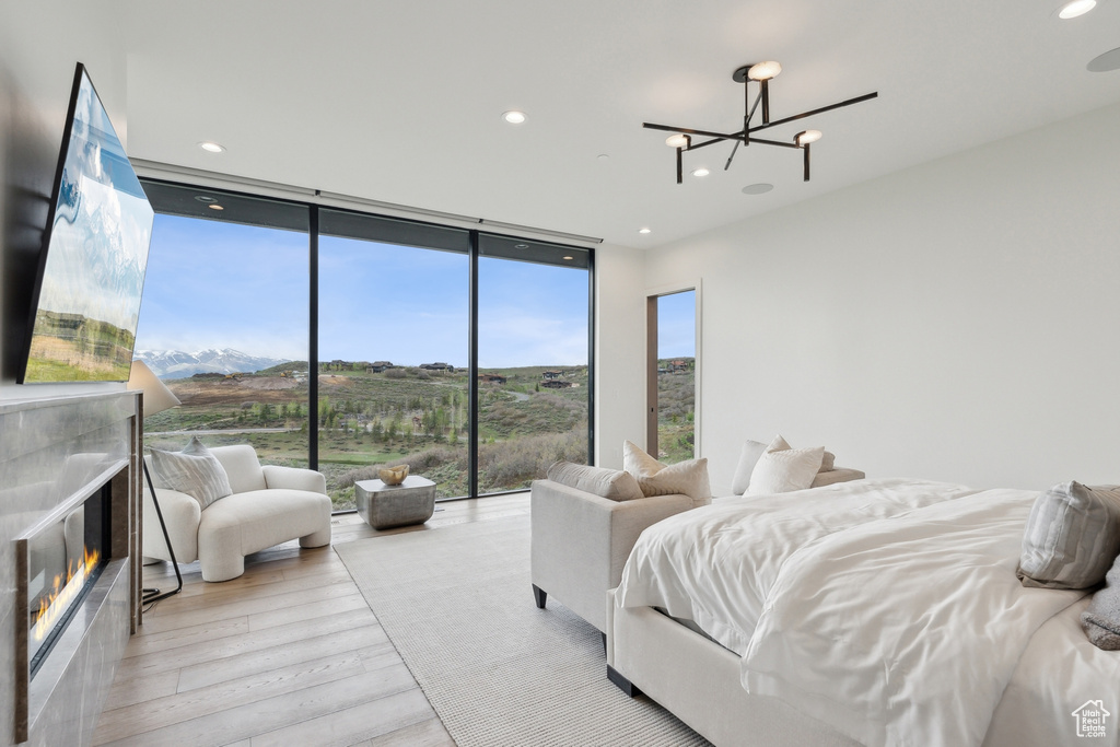 Bedroom featuring expansive windows, light wood-style floors, a chandelier, a glass covered fireplace, and recessed lighting