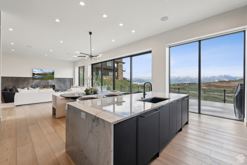Kitchen with a sink, a large island with sink, modern cabinets, recessed lighting, and light stone countertops