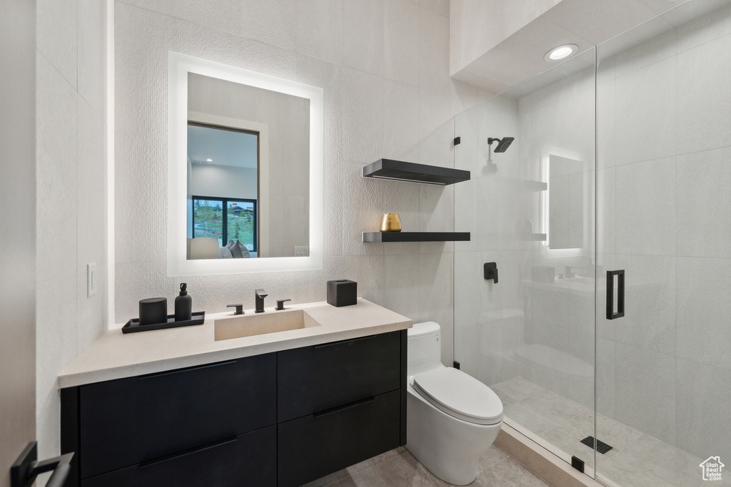 Bathroom featuring toilet, a stall shower, vanity, tile walls, and tile patterned flooring