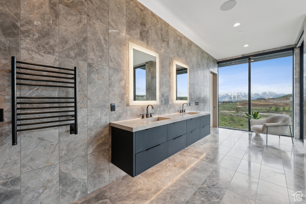 Full bath with radiator heating unit, a towel warming rack, double vanity, a wall of windows, and tile walls