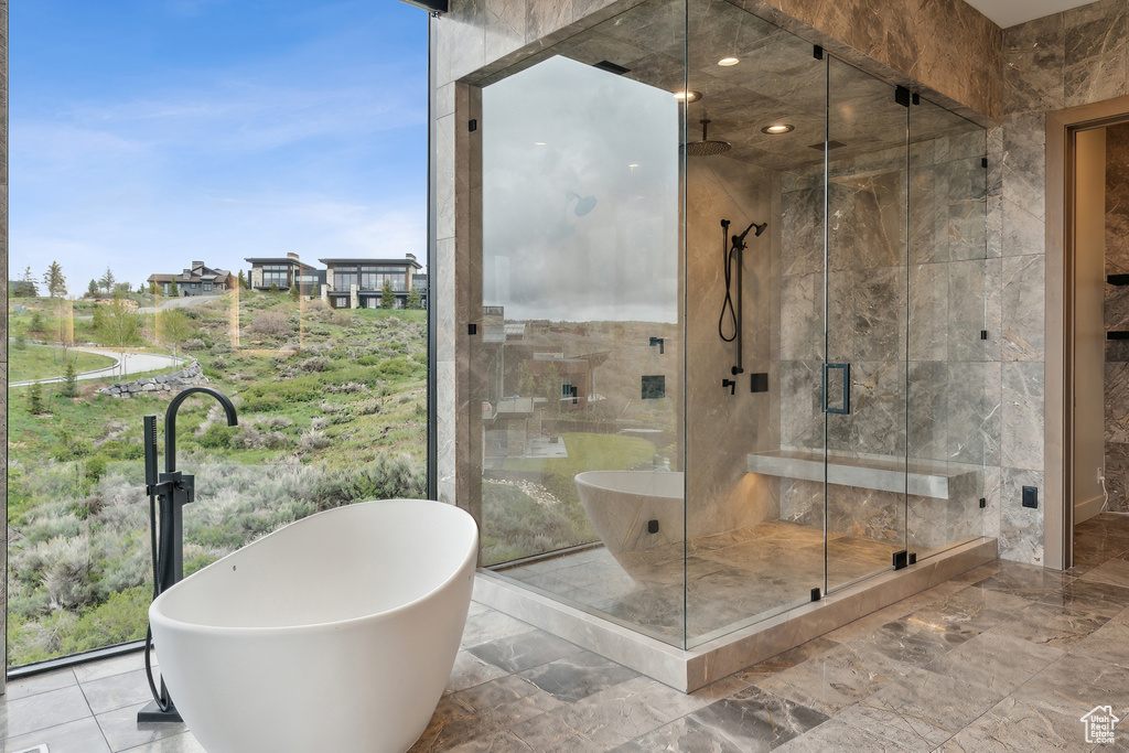 Bathroom featuring a soaking tub, marble tiled floors, a stall shower, and tile walls
