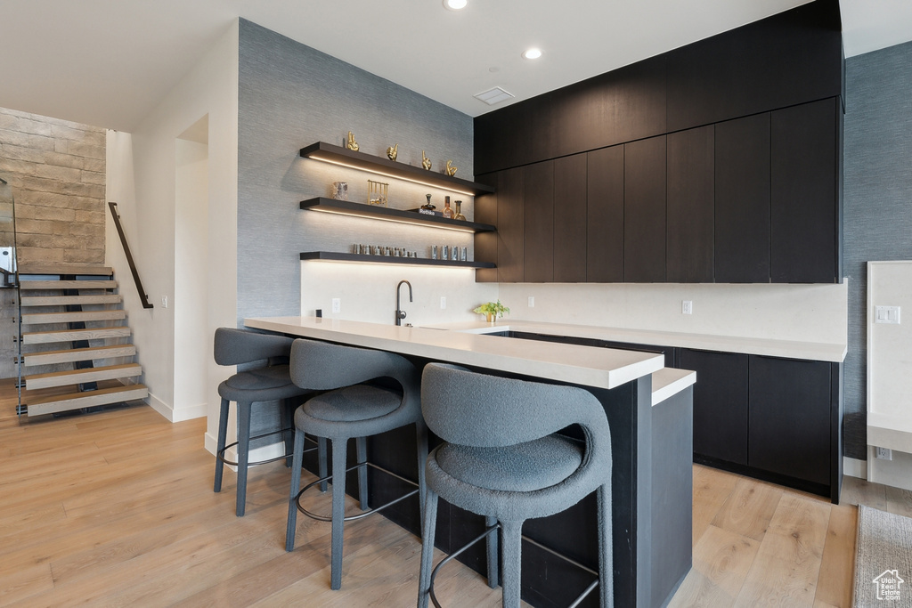 Indoor wet bar with light wood-type flooring, stairs, baseboards, and recessed lighting