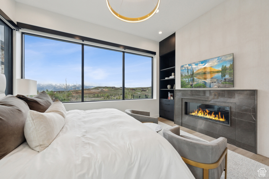 Bedroom with wood finished floors, a glass covered fireplace, and recessed lighting