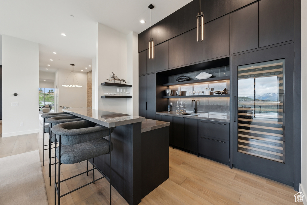 Indoor wet bar with light wood-style flooring, beverage cooler, recessed lighting, decorative light fixtures, and baseboards