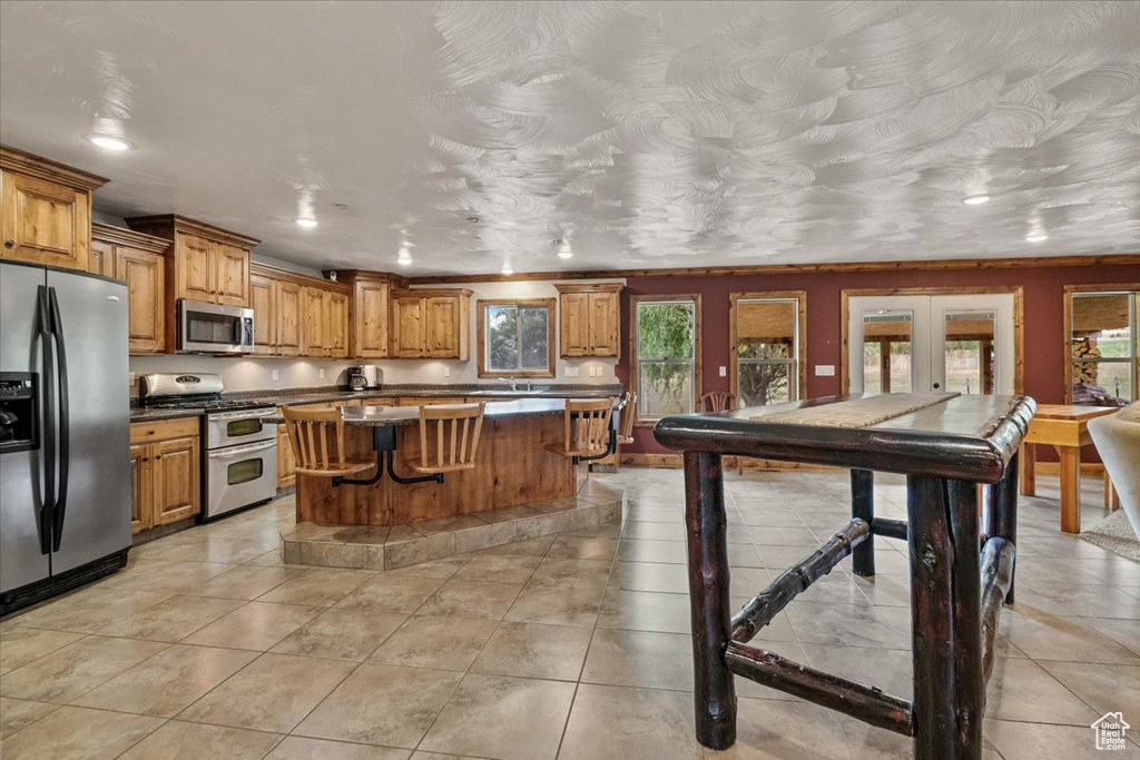 Kitchen with french doors, light tile patterned floors, a breakfast bar area, a kitchen island, and appliances with stainless steel finishes