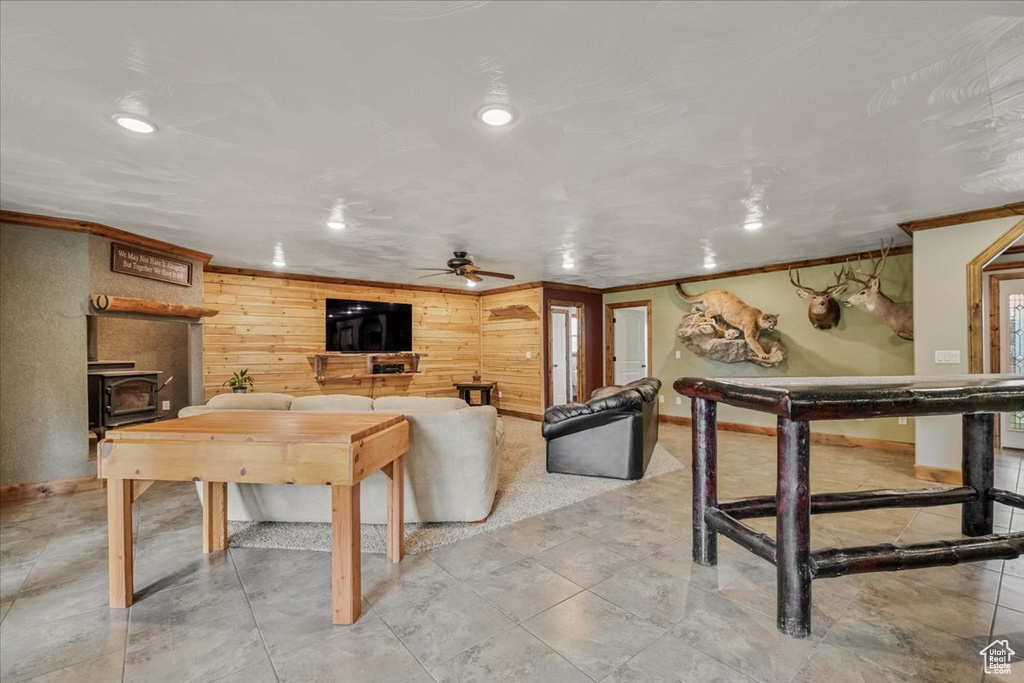 Living room featuring ceiling fan, wood walls, a wood stove, and crown molding