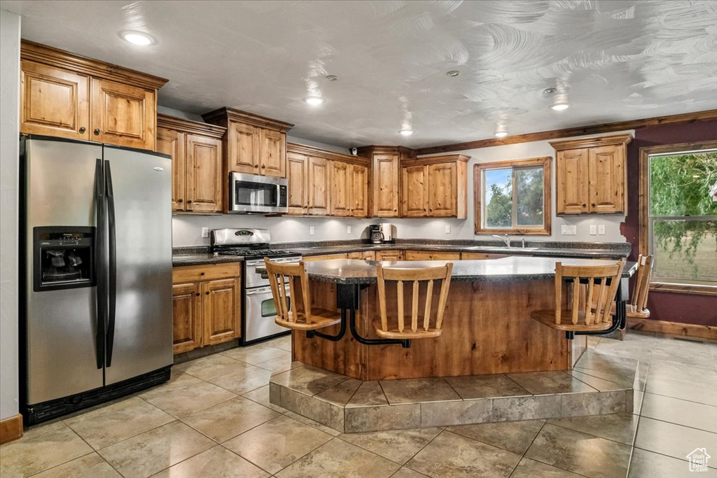 Kitchen with a center island, sink, stainless steel appliances, a kitchen breakfast bar, and light tile patterned flooring