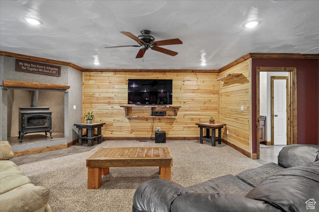 Carpeted living room with a wood stove, ceiling fan, ornamental molding, and wood walls
