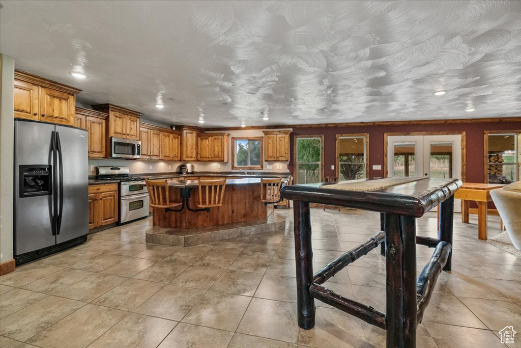 Kitchen featuring a breakfast bar, a center island, french doors, light tile patterned floors, and appliances with stainless steel finishes