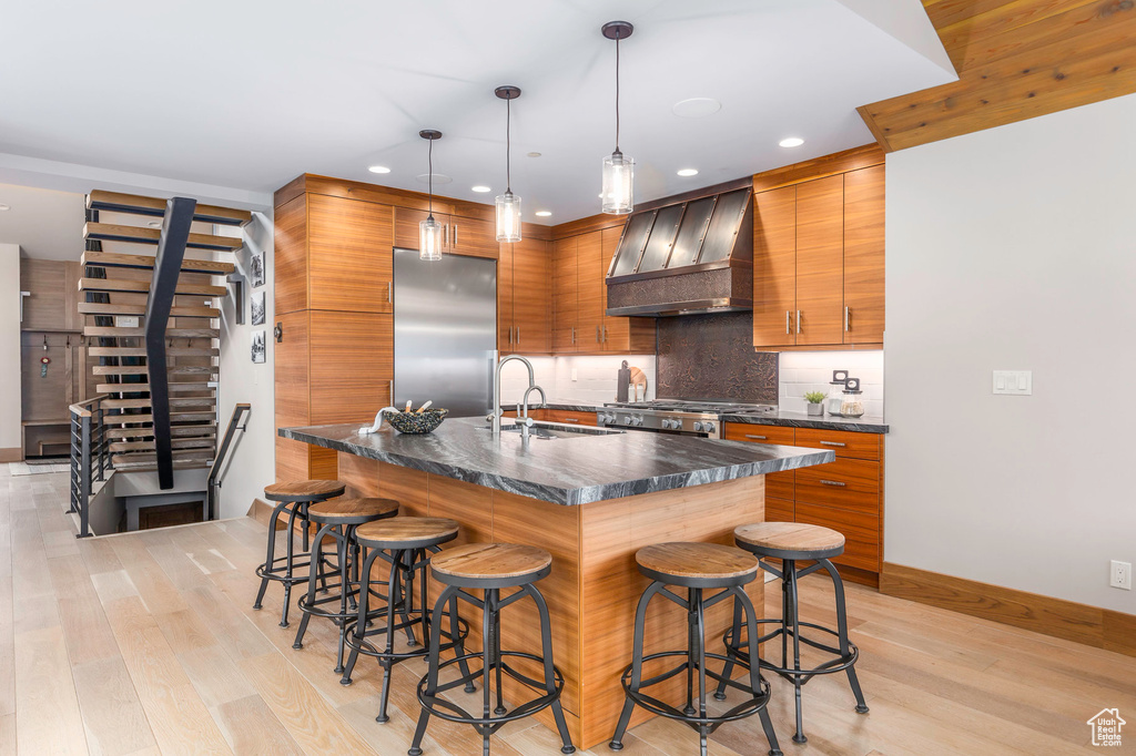 Kitchen with ventilation hood, high end fridge, light wood-type flooring, a kitchen breakfast bar, and recessed lighting
