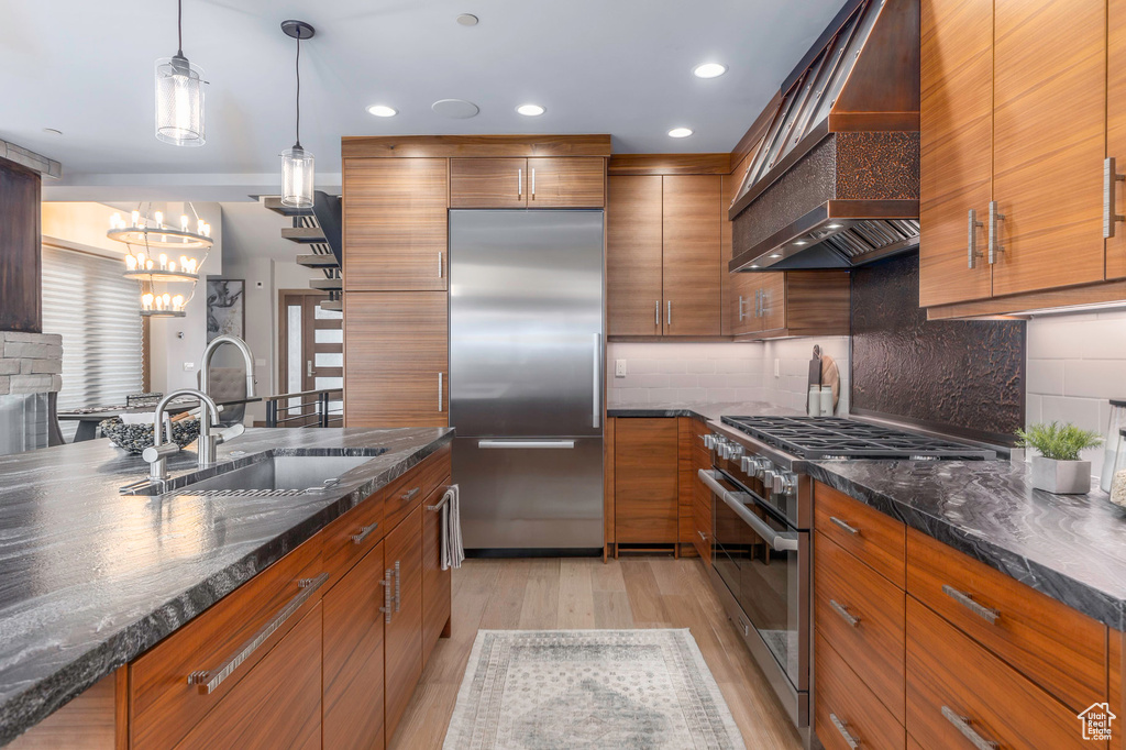Kitchen with premium appliances, wall chimney range hood, a sink, brown cabinets, and recessed lighting