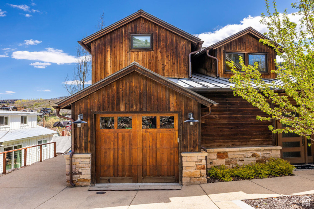 View of front facade with a standing seam roof, stone siding, metal roof, and a garage