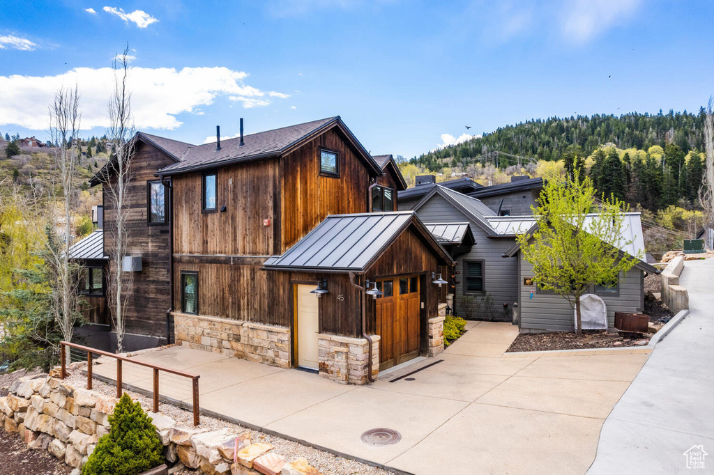 View of front of property featuring a standing seam roof, metal roof, stone siding, and a wooded view