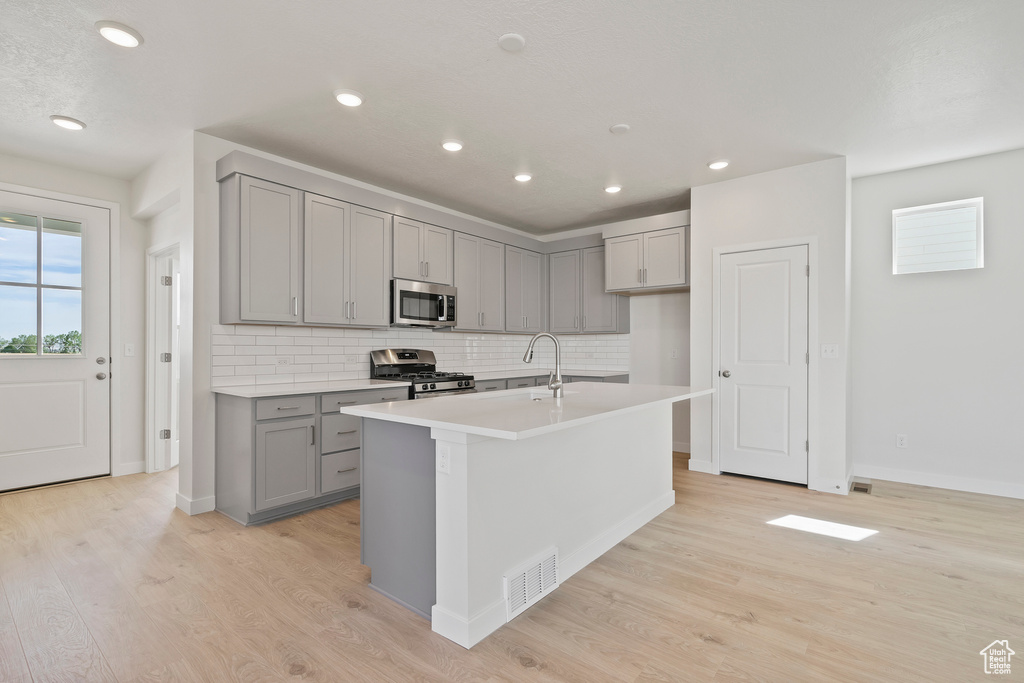 Kitchen featuring appliances with stainless steel finishes, gray cabinetry, tasteful backsplash, light wood finished floors, and recessed lighting
