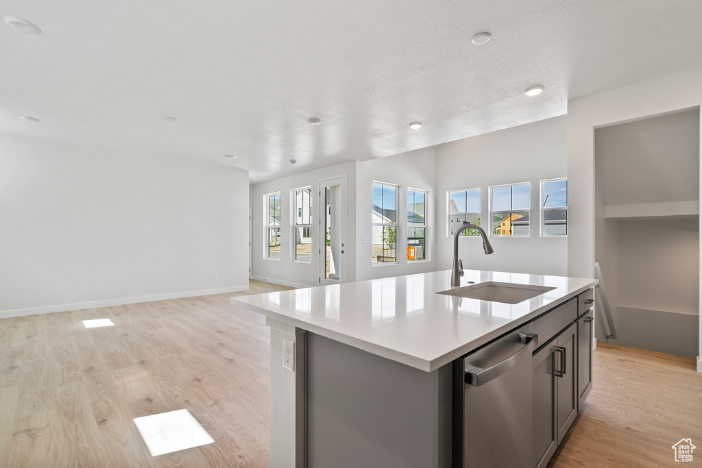 Kitchen featuring a sink, stainless steel dishwasher, light wood-style floors, open floor plan, and a kitchen island with sink