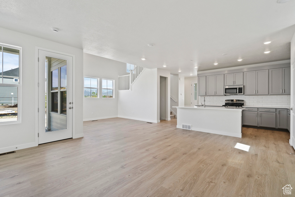 Kitchen with gray cabinetry, appliances with stainless steel finishes, light wood-type flooring, baseboards, and recessed lighting