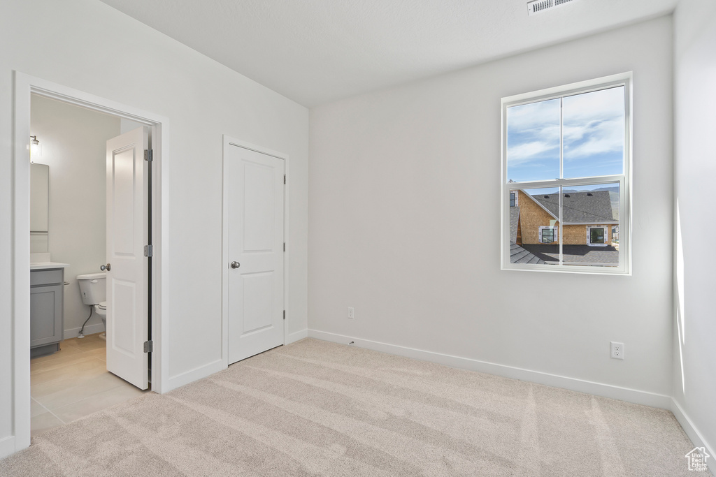 Unfurnished bedroom with light carpet, baseboards, and ensuite bathroom