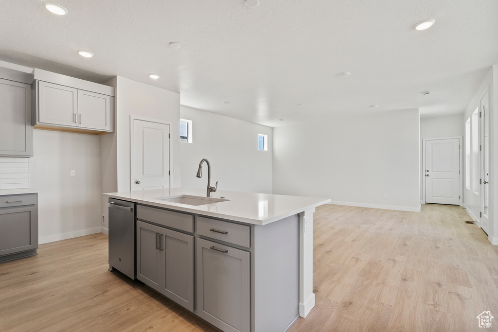 Kitchen featuring a sink, gray cabinets, stainless steel dishwasher, light wood-style flooring, and light countertops