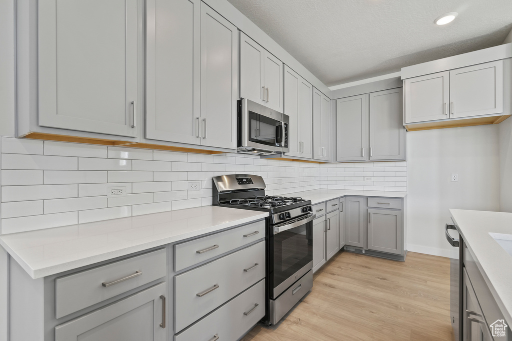 Kitchen featuring appliances with stainless steel finishes, gray cabinets, light wood-style flooring, and light countertops