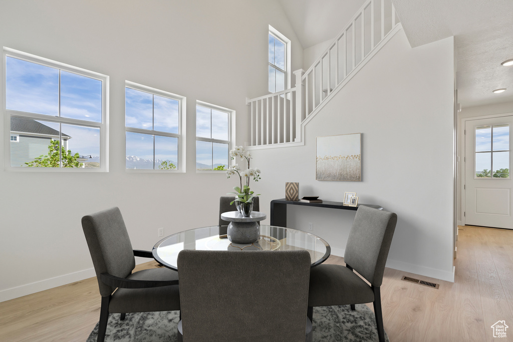 Dining area with light wood finished floors, baseboards, and a towering ceiling
