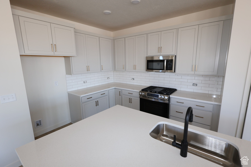 Kitchen featuring gray cabinetry, light countertops, decorative backsplash, stainless steel appliances, and a sink