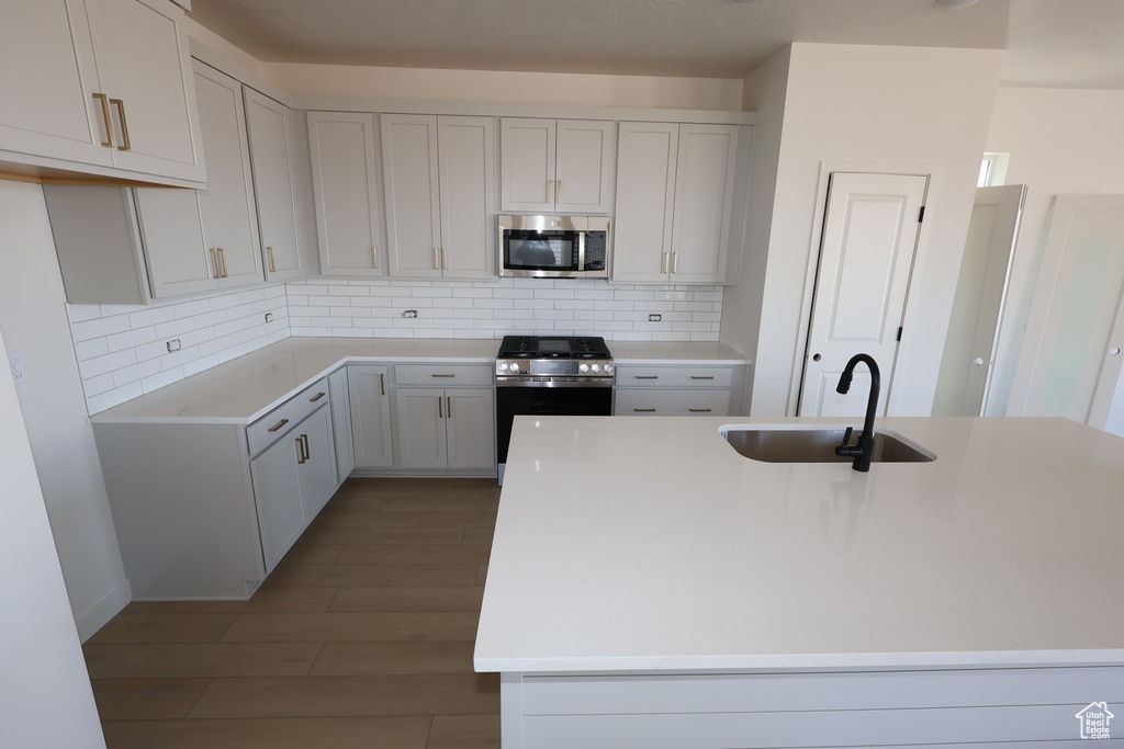 Kitchen with a kitchen island with sink, a sink, stainless steel appliances, light countertops, and backsplash
