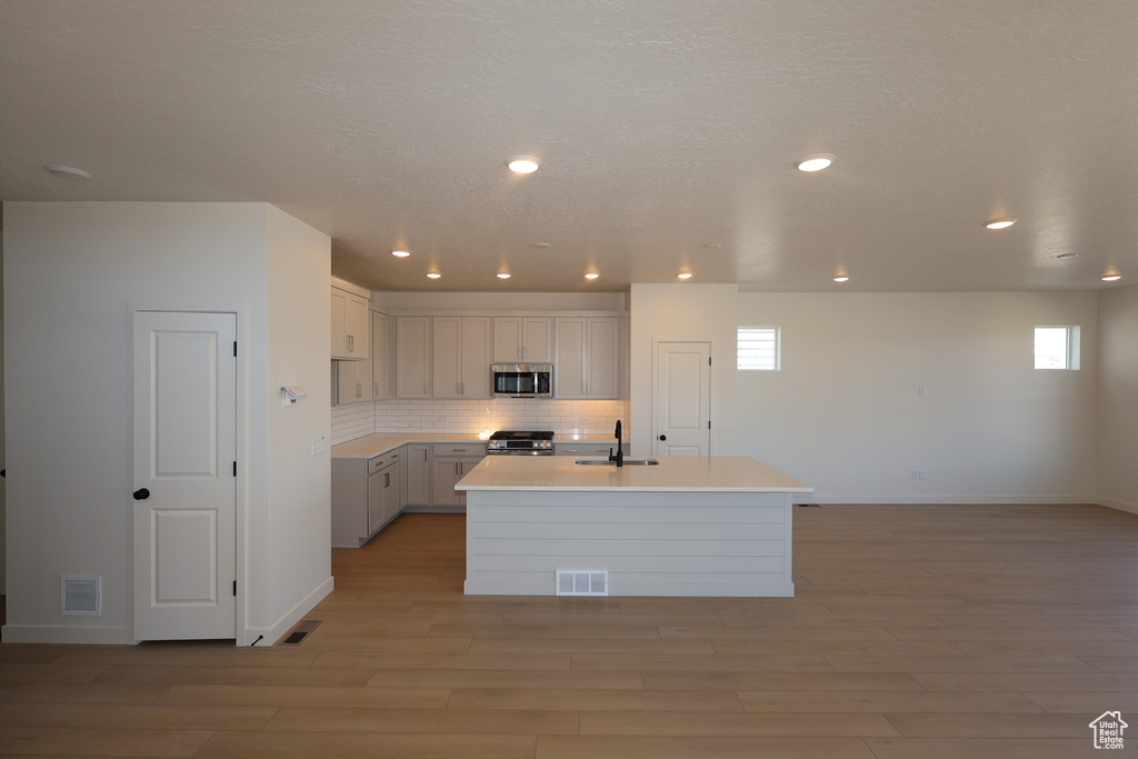 Kitchen with light wood finished floors, visible vents, backsplash, appliances with stainless steel finishes, and a sink