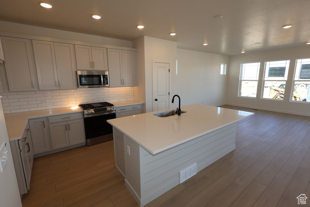 Kitchen with backsplash, appliances with stainless steel finishes, wood finished floors, and a sink