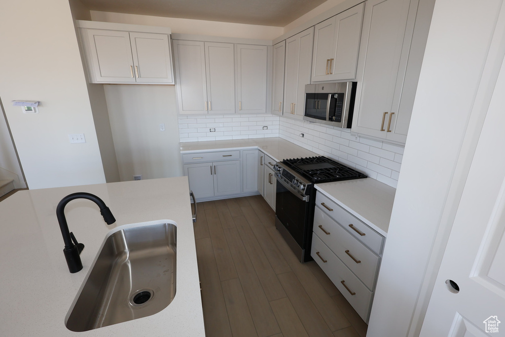Kitchen featuring decorative backsplash, dark wood-style flooring, stainless steel appliances, and a sink