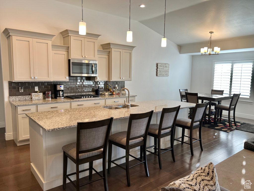 Kitchen featuring decorative light fixtures, sink, an island with sink, and dark wood-type flooring