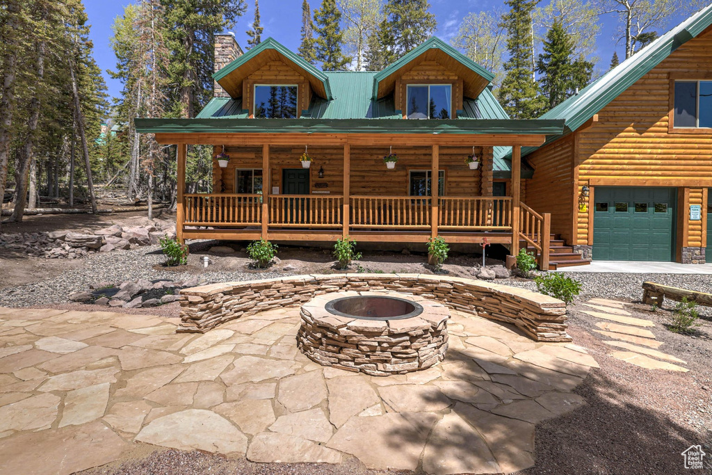 Log cabin with covered porch, a fire pit, and a garage