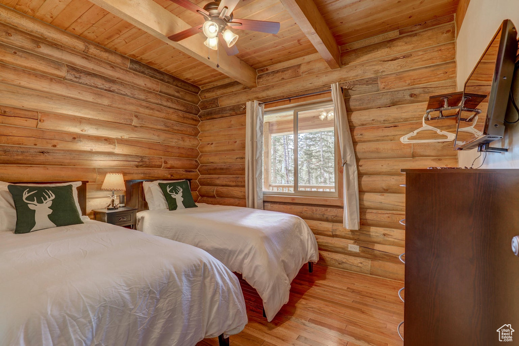 Bedroom with wooden ceiling, light hardwood / wood-style flooring, ceiling fan, rustic walls, and beamed ceiling