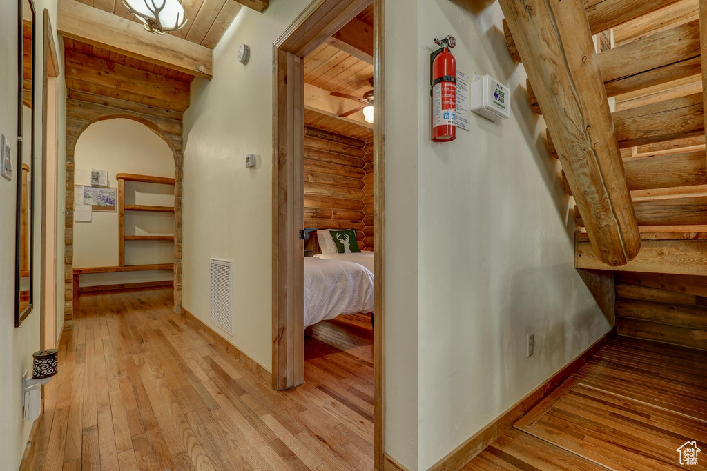 Corridor with beam ceiling, wood ceiling, rustic walls, and light hardwood / wood-style flooring