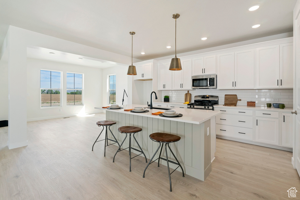 Kitchen featuring stainless steel appliances, backsplash, a breakfast bar area, light wood-style flooring, and recessed lighting