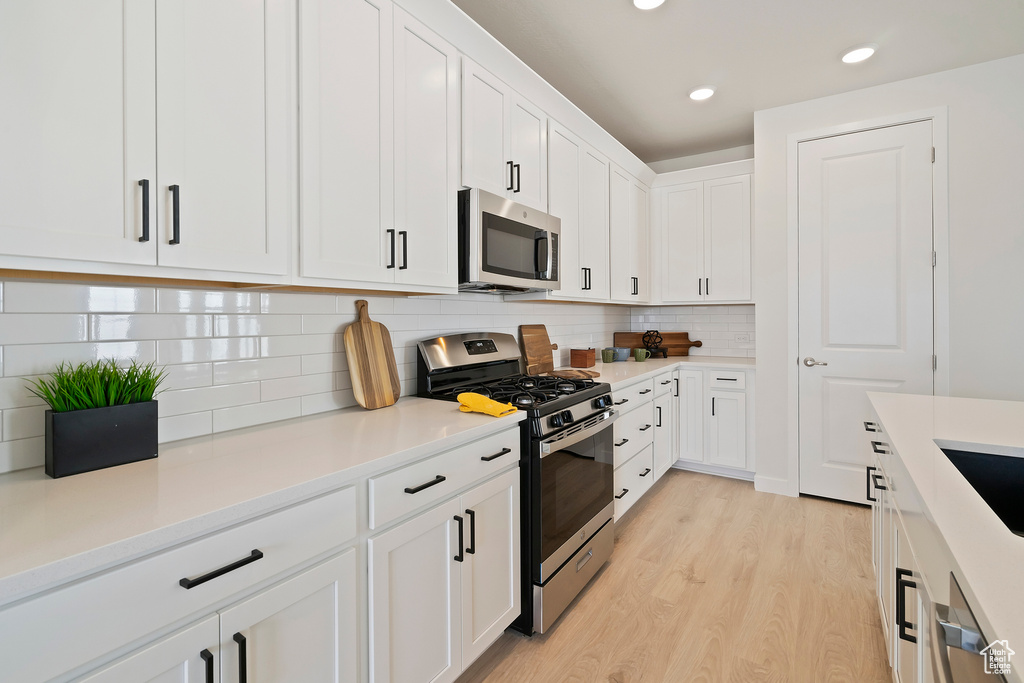 Kitchen with appliances with stainless steel finishes, light wood finished floors, white cabinets, recessed lighting, and decorative backsplash