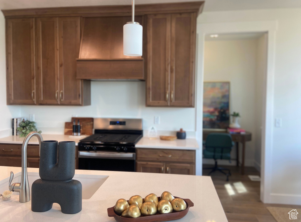 Kitchen with gas range, sink, range hood, pendant lighting, and wood-type flooring