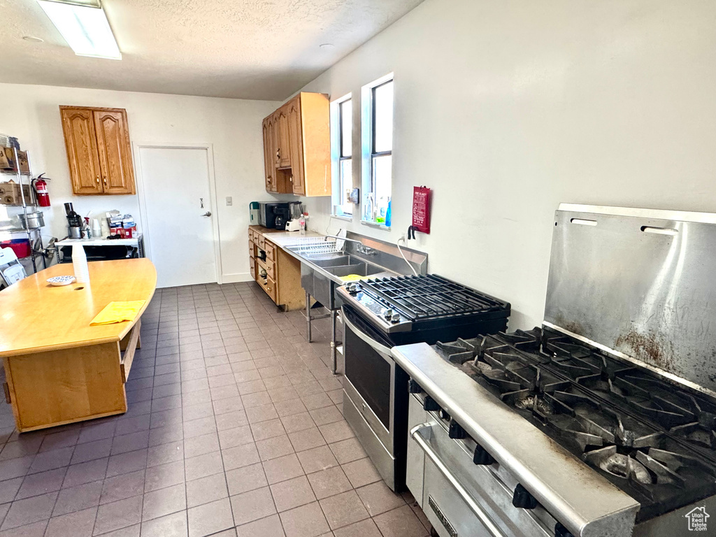 Kitchen with stainless steel gas range oven, light countertops, tile patterned flooring, a textured ceiling, and range