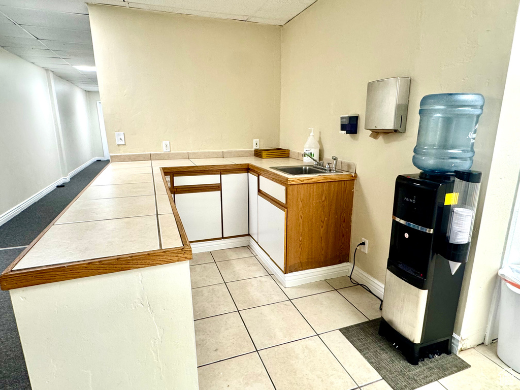 Kitchen with a drop ceiling, light tile patterned flooring, a sink, a peninsula, and white cabinetry