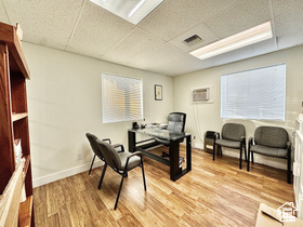 Office area featuring a drop ceiling, light wood finished floors, a wall mounted AC, and baseboards