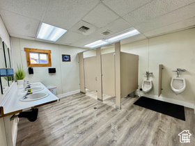 Bathroom featuring wood finished floors, a paneled ceiling, double vanity, toilet, and baseboards