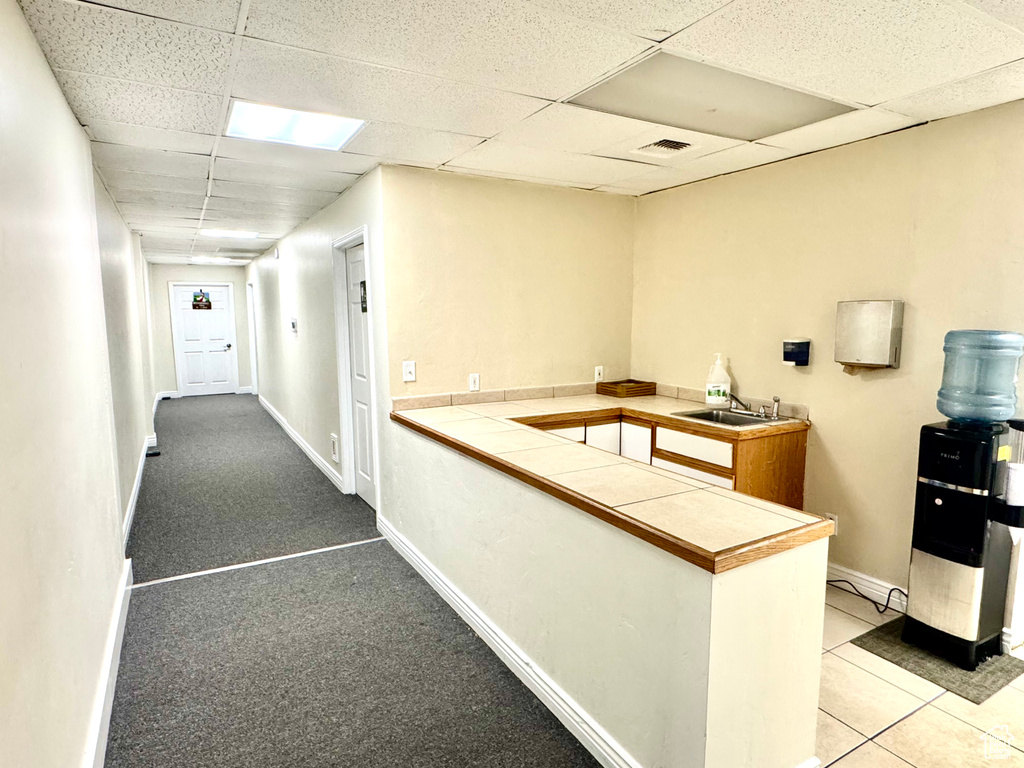 Hallway featuring a paneled ceiling, baseboards, and a sink