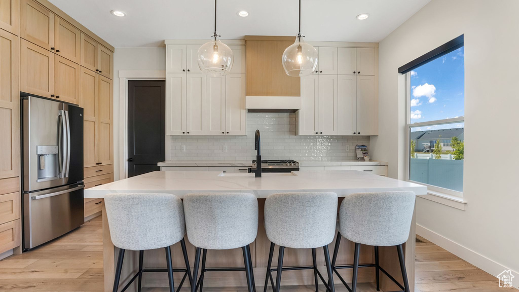 Kitchen with stainless steel fridge, decorative backsplash, an island with sink, a kitchen breakfast bar, and recessed lighting