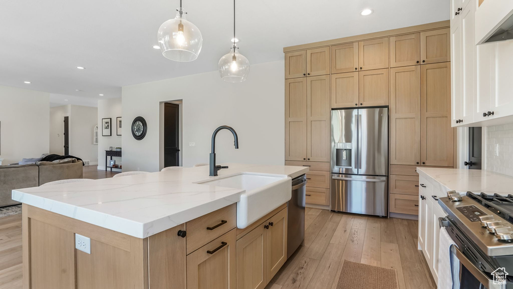 Kitchen with stainless steel appliances, a sink, light wood-style floors, light brown cabinetry, and light stone countertops