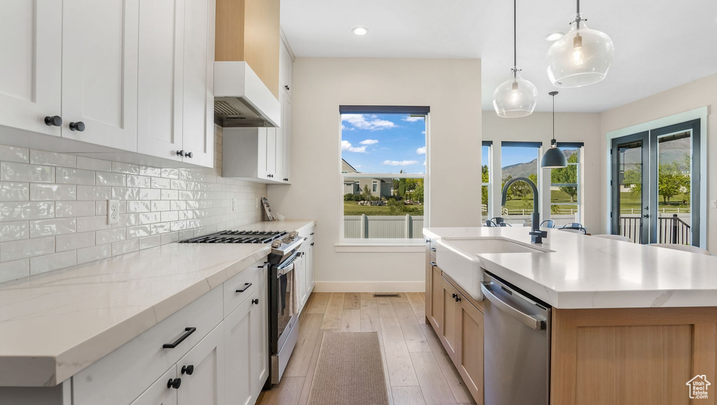 Kitchen featuring stainless steel appliances, a sink, light wood-style flooring, decorative backsplash, and a kitchen island with sink