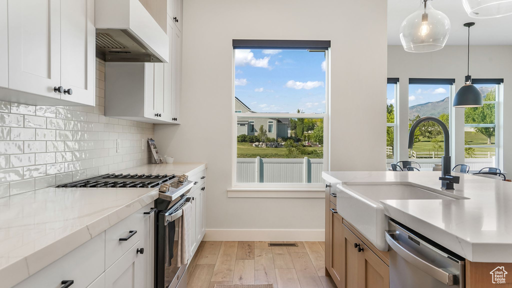 Kitchen with stainless steel appliances, premium range hood, light wood-style flooring, decorative backsplash, and baseboards