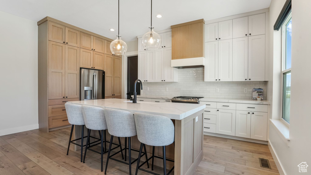 Kitchen with stainless steel fridge, tasteful backsplash, light wood finished floors, a breakfast bar area, and recessed lighting