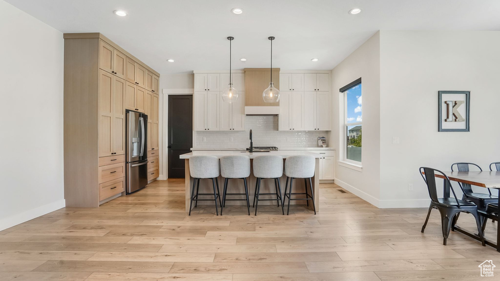 Kitchen with stainless steel fridge with ice dispenser, a kitchen breakfast bar, light countertops, light wood finished floors, and a center island with sink