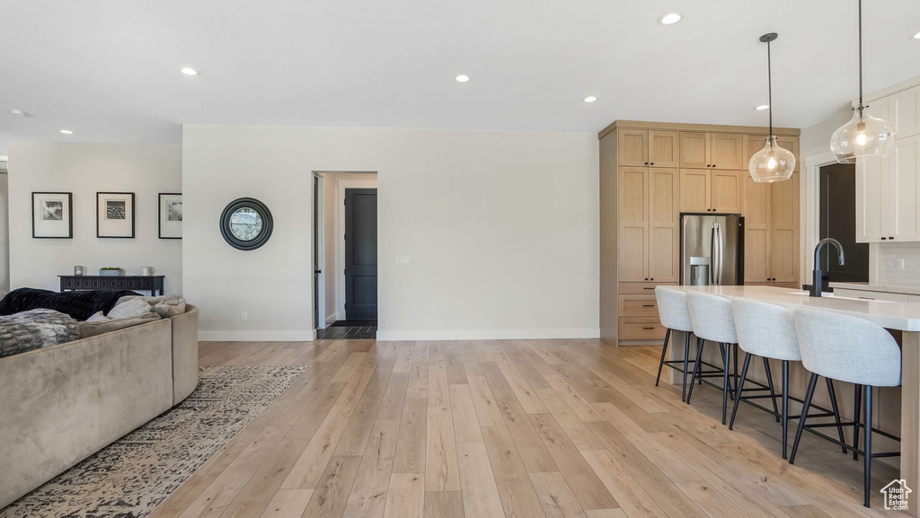 Kitchen with stainless steel refrigerator with ice dispenser, open floor plan, light countertops, a kitchen bar, and a sink