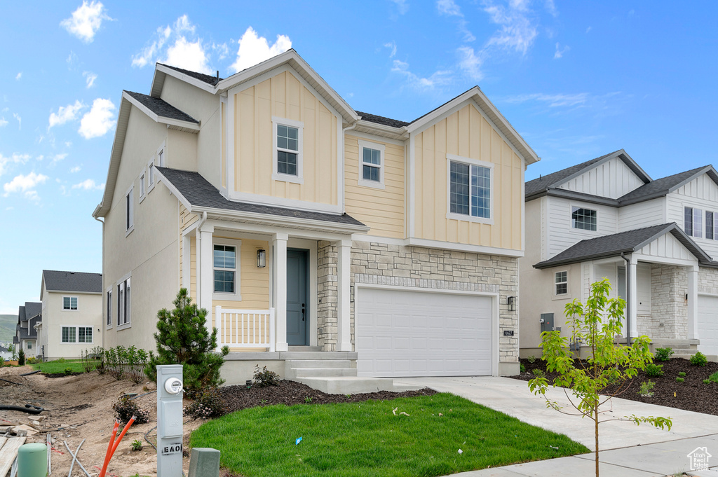View of front of home featuring board and batten siding, concrete driveway, a garage, stone siding, and a front lawn