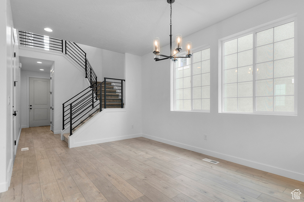 Unfurnished dining area featuring a chandelier, baseboards, stairs, light wood-style flooring, and recessed lighting